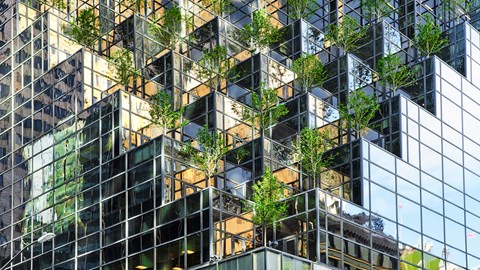 Glass building with staggered terraces featuring green trees.